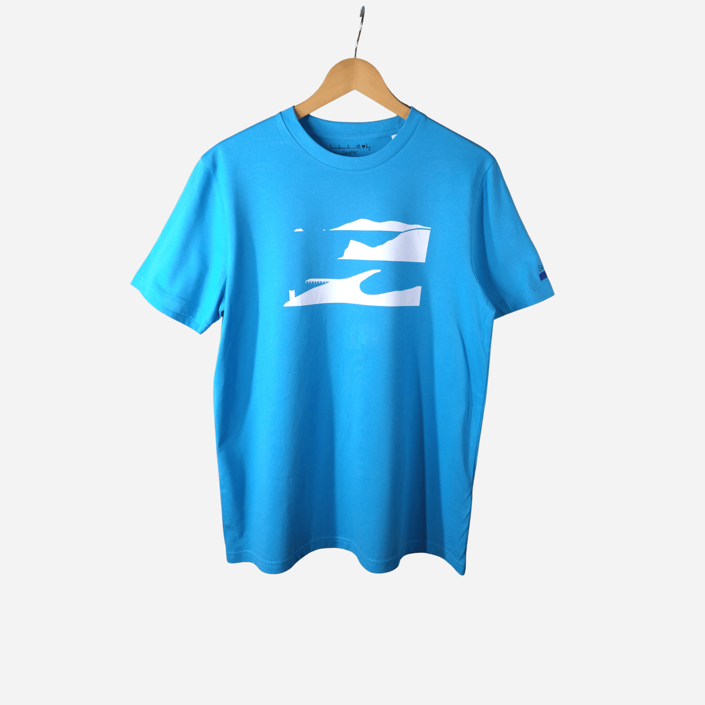 Aqua blue organic cotton t-shirt featuring a minimalist white screen-printed 'Ness View' landscape design, displayed on a wooden hanger.
